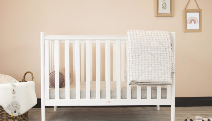 A cozy classic crib in a light baby room with toys on a soft carpet and a woven basket on the corner